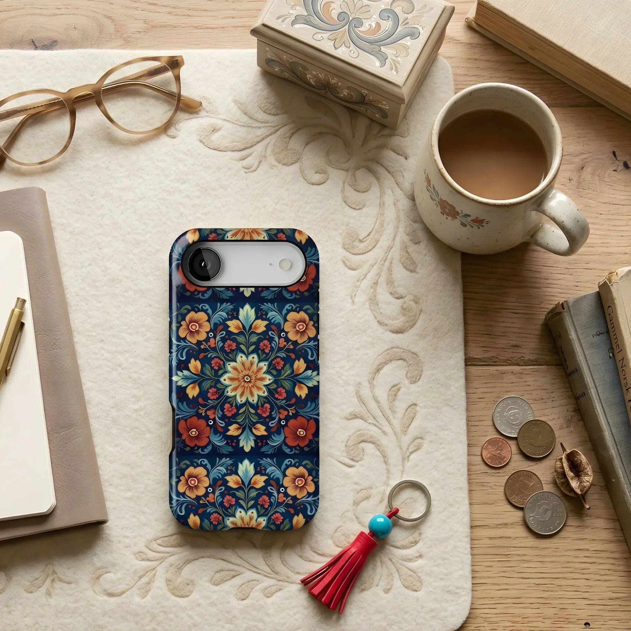 Norwegian Rosemaling Floral phone case on a textured surface with a mug, glasses, and coins.